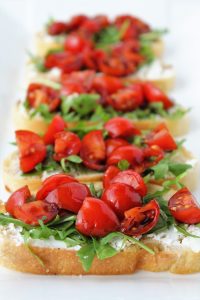 bread with goat cheese spread arugula tomatoes and balsamic on a platter