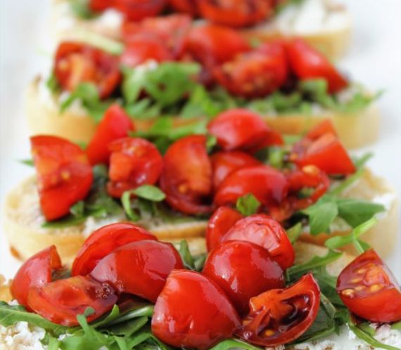bread with goat cheese spread arugula tomatoes and balsamic on a platter