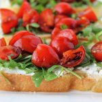 bread with goat cheese spread arugula tomatoes and balsamic on a platter