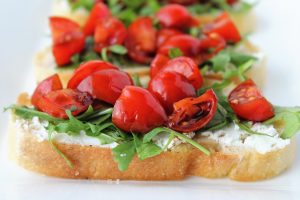 bread with goat cheese spread arugula tomatoes and balsamic on a platter