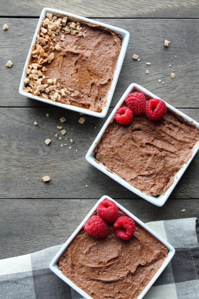 white square bowl filled with chocolate mousse and toffee bits garnished with fresh raspberries