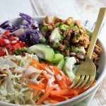 chicken and veggies in a bowl with dressing and fork