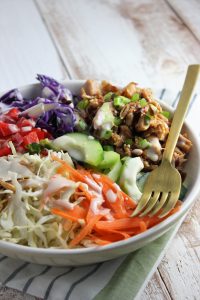 chicken and veggies in a bowl with dressing and fork