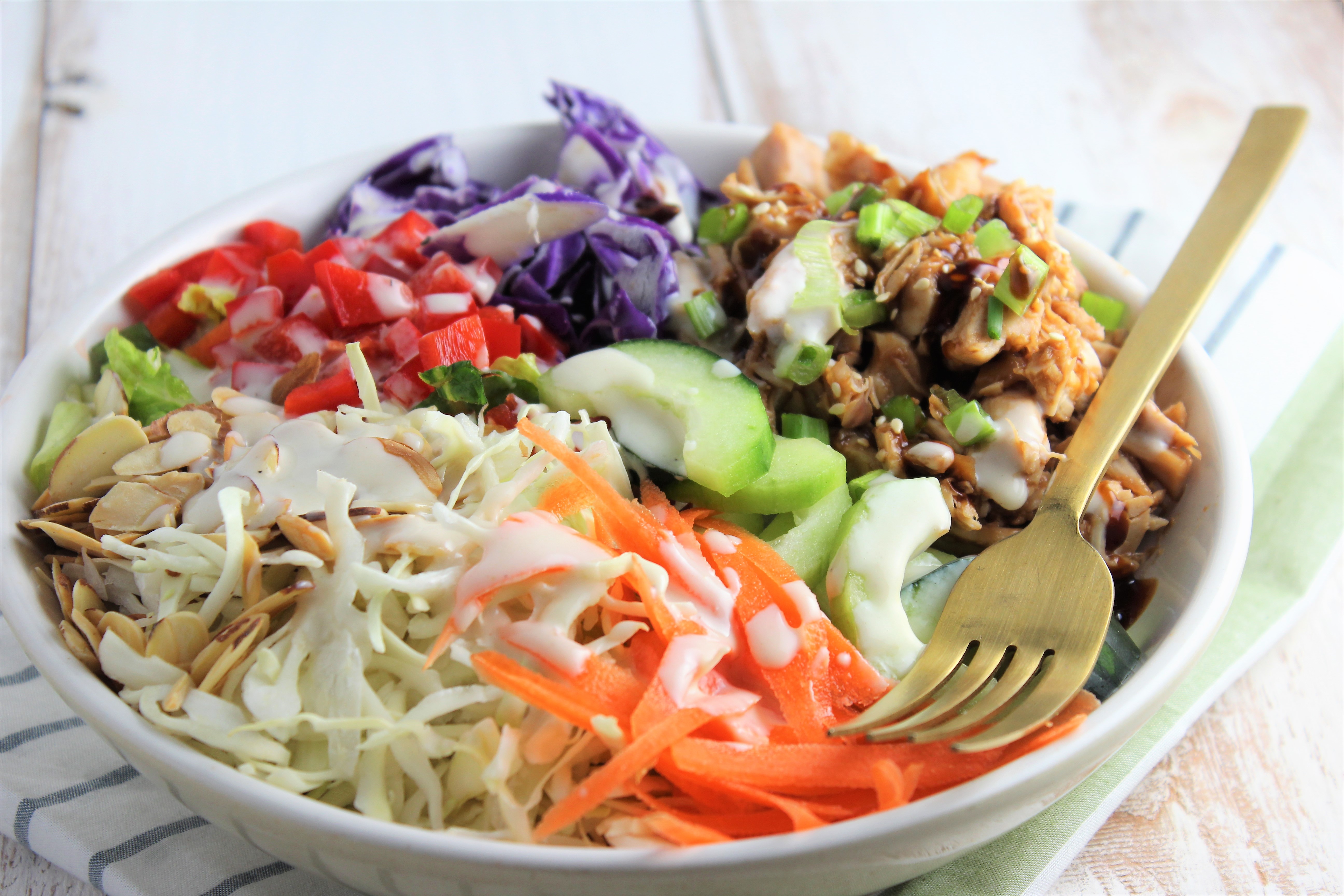 chicken and veggies in a bowl with dressing and fork