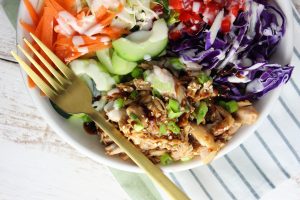 chicken and veggies in a bowl with dressing and fork