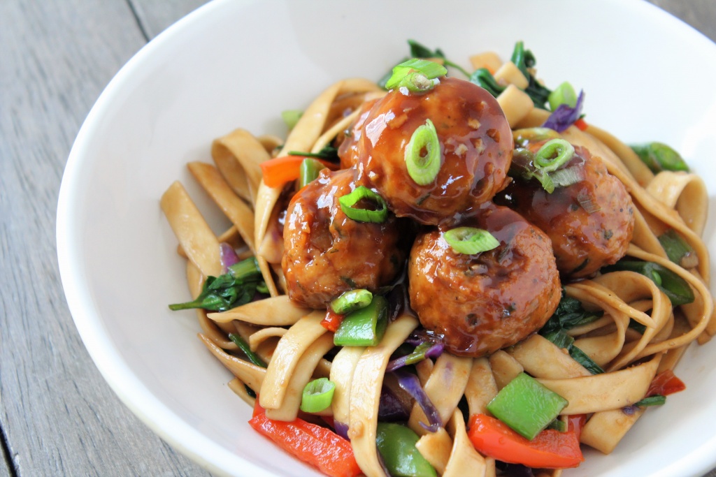 white bowl lo mein noodles and veggies with hoisin glazed meatballs with wood backdrop