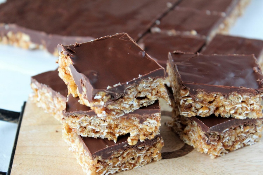 rice cereal oats bars with almond butter stacked on a cutting board, chocolate frosting on top.