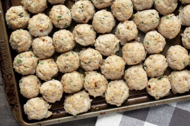 baking sheet pan with baked chicken meatballs laying on wood backdrop and towel.