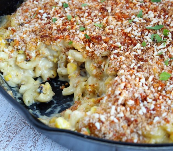 mac and cheese with corn in a cast iron skillet topped with cotija cheese and bread crumbs and spices