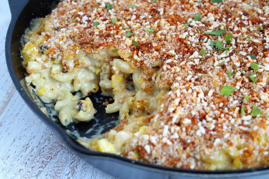 mac and cheese with corn in a cast iron skillet topped with cotija cheese and bread crumbs and spices