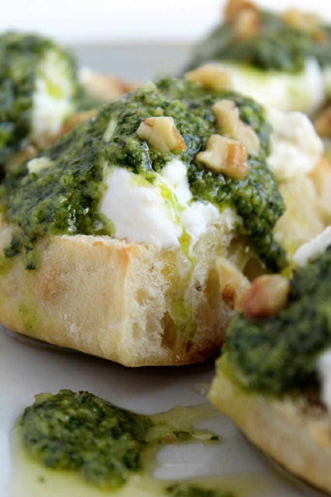 square bread on round plate topped with white cheese, honey, olive oil, fresh basil pesto and walnuts.