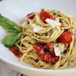 pasta in white bowl with basil, cherry tomatoes, parm and pesto sauce