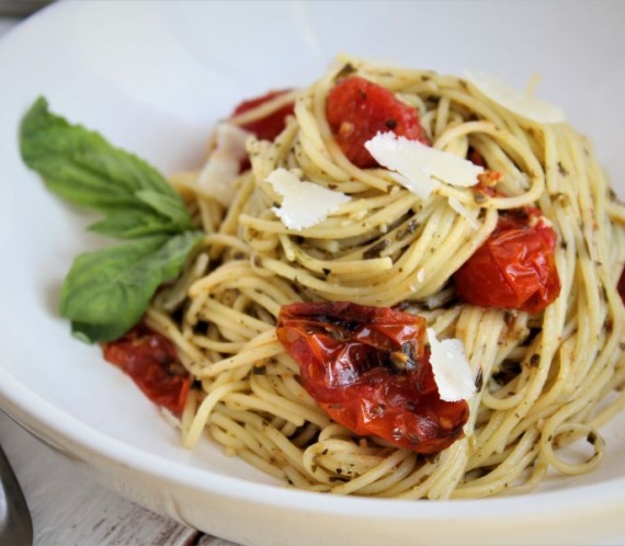 pasta in white bowl with basil, cherry tomatoes, parm and pesto sauce